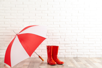 Photo of Beautiful colorful umbrella and rubber boots near white brick wall. Space for text