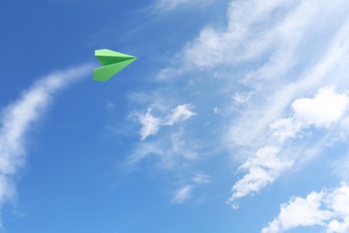 Image of Green paper plane flying in blue sky with clouds