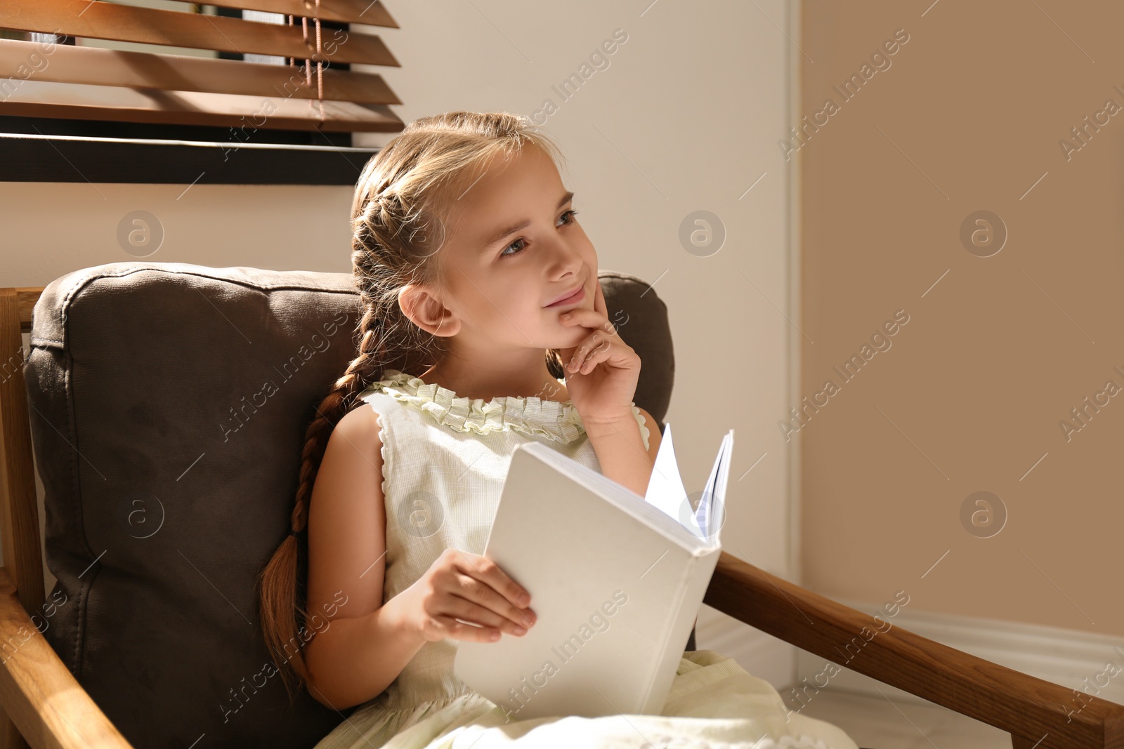 Photo of Little girl reading book in armchair at home