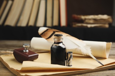 Feather pen, bottle of ink, notebook and parchment scroll on wooden table