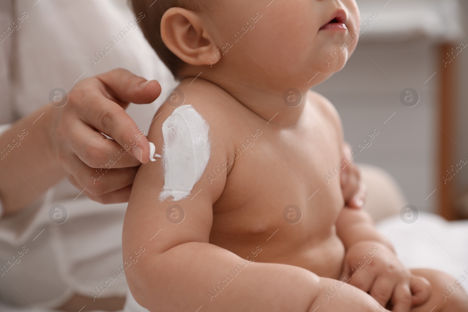 Photo of Mother applying moisturizing cream on her little baby at home, closeup