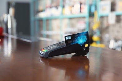 Photo of Credit card machine for non cash payment on wooden counter in cafe. Space for text