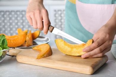 Woman slicing fresh ripe melon on light table