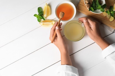 Photo of Woman drinking delicious ginger tea with honey at white wooden table, top view. Space for text