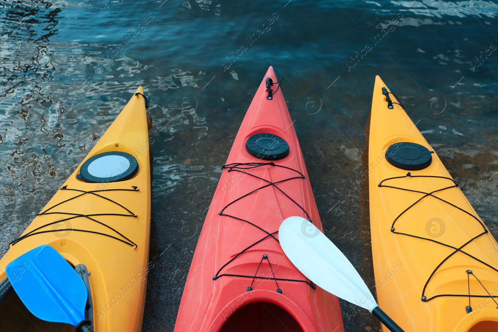 Photo of Modern kayaks with paddles on beach near river, above view. Summer camp activity