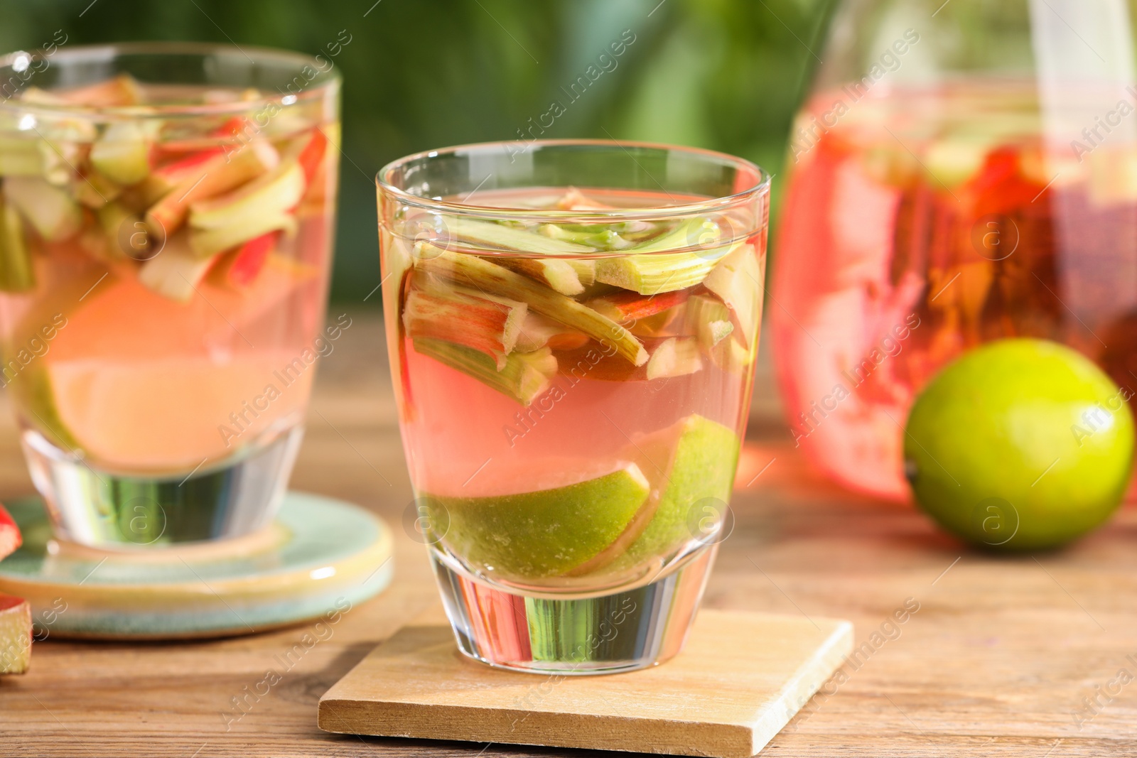 Photo of Tasty rhubarb cocktail with lime on wooden table outdoors, closeup