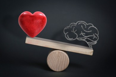 Image of Choosing between logic and emotions. Miniature wooden seesaw with heart and brain against black background