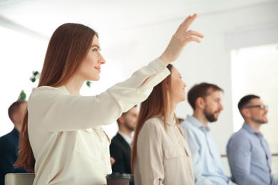 Photo of Young woman raising hand to ask question at business training indoors
