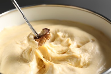 Dipping nut into fondue pot with melted cheese, closeup