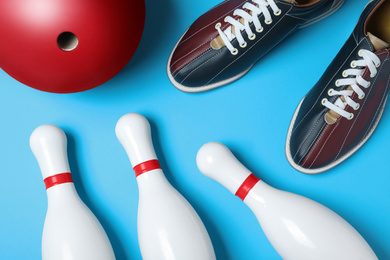 Photo of Bowling ball, shoes and pins on light blue background, flat lay