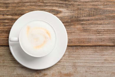 Tasty cappuccino in coffee cup on wooden table, top view. Space for text