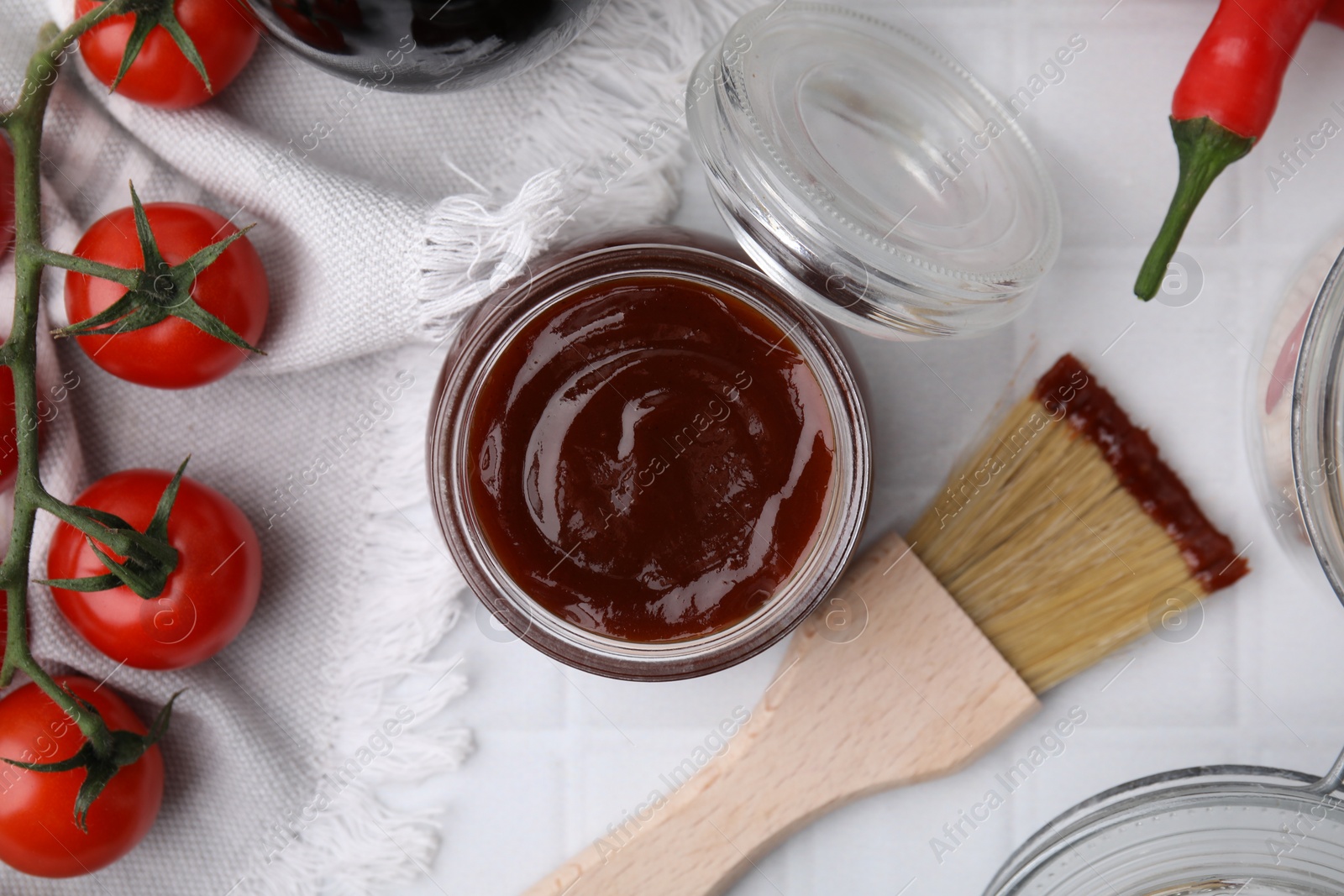 Photo of Marinade in jar, ingredients and basting brush on white tiled table, flat lay