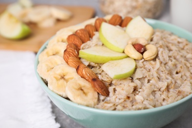Photo of Bowl of delicious oatmeal with fruits and nuts on table, closeup