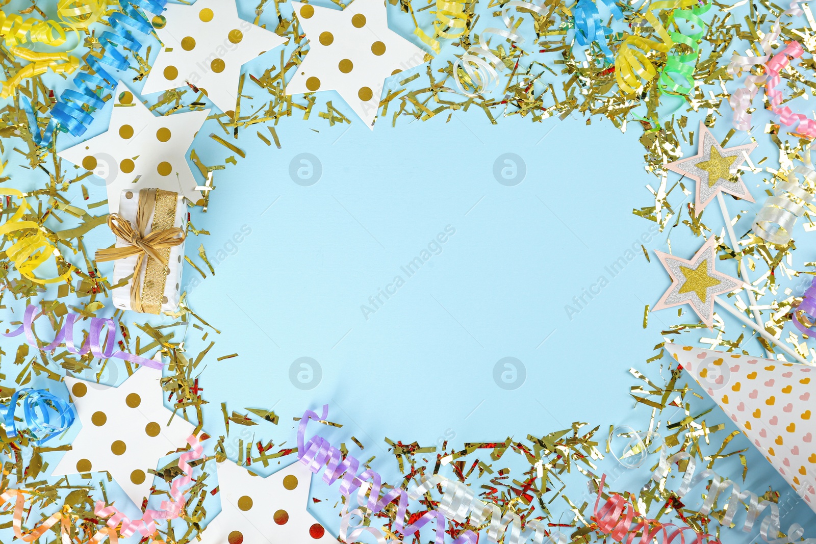 Photo of Frame of serpentine streamers and other party accessories on light blue background, flat lay. Space for text