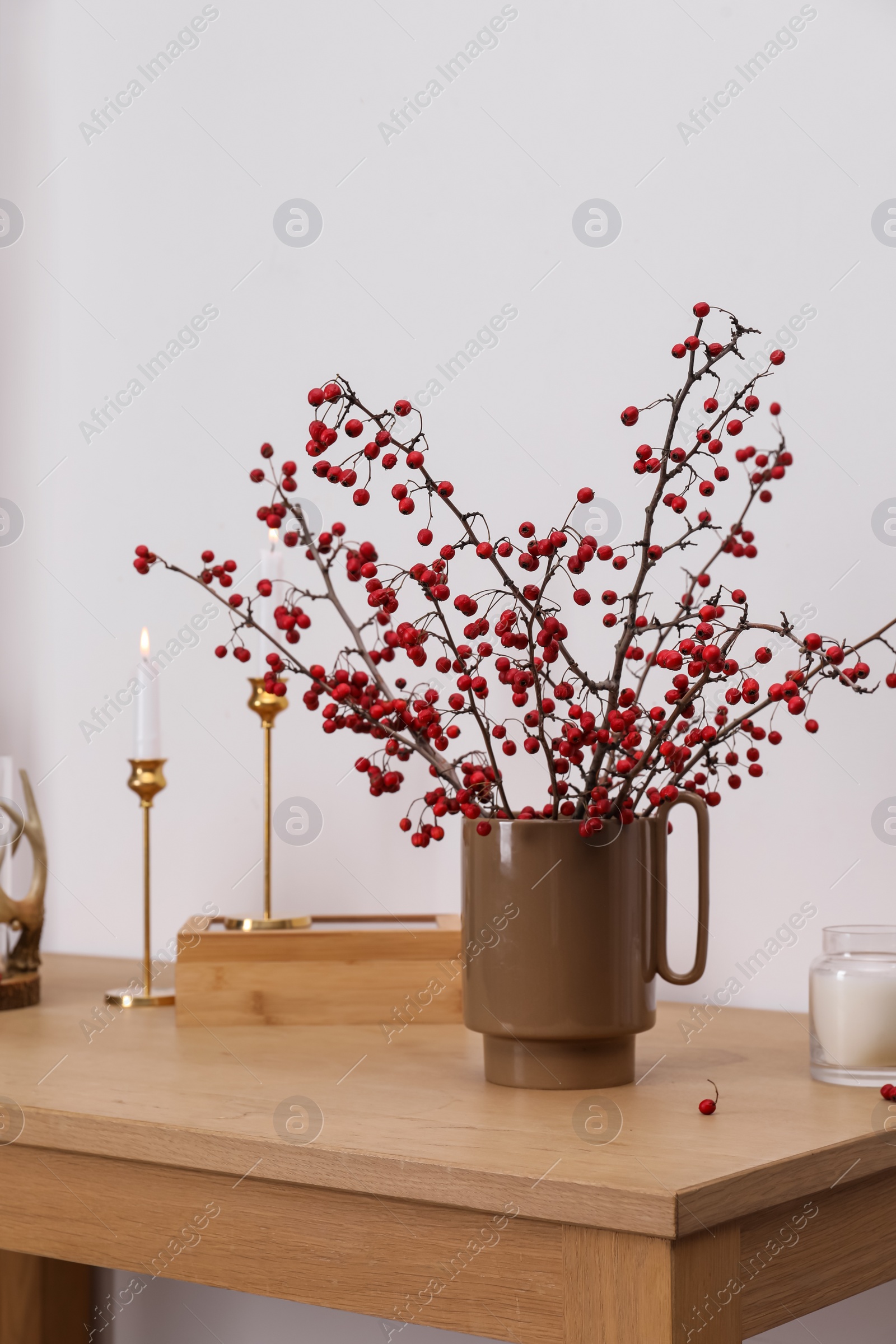 Photo of Hawthorn branches with red berries, box and candles on wooden table indoors