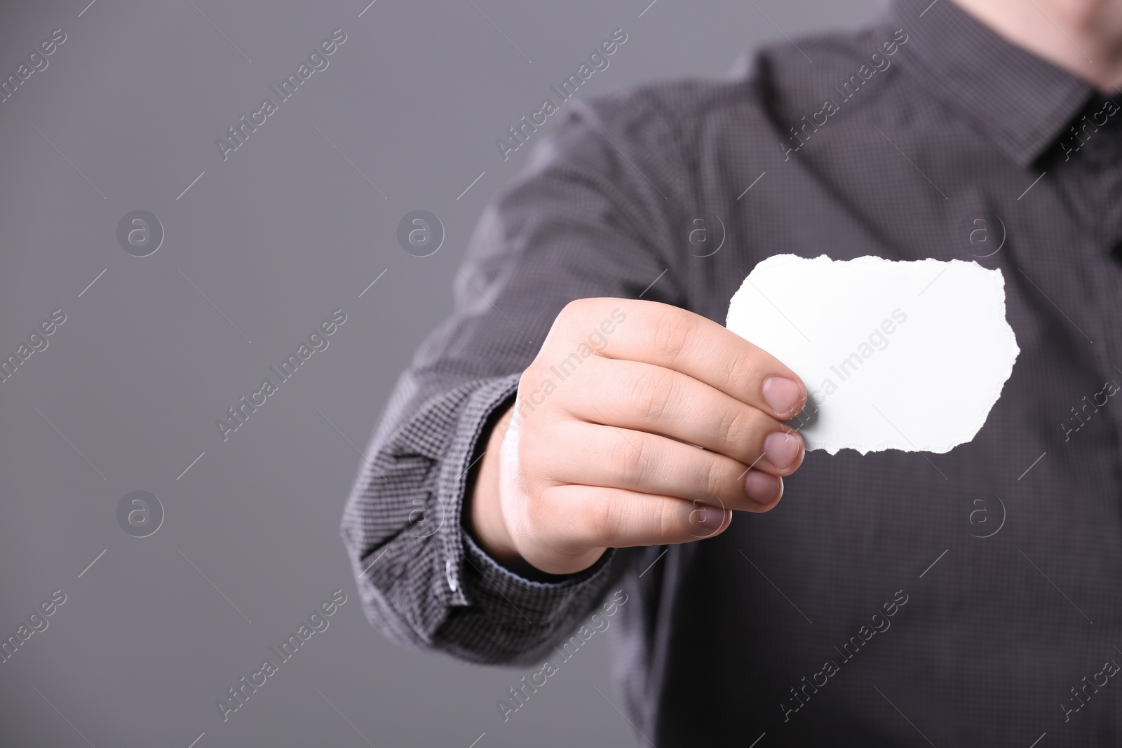 Photo of Closeup of man holding sheet of torn paper on grey background, focus on hand. Mockup for design