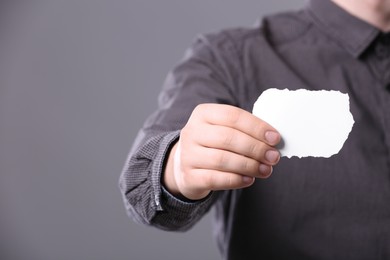 Closeup of man holding sheet of torn paper on grey background, focus on hand. Mockup for design