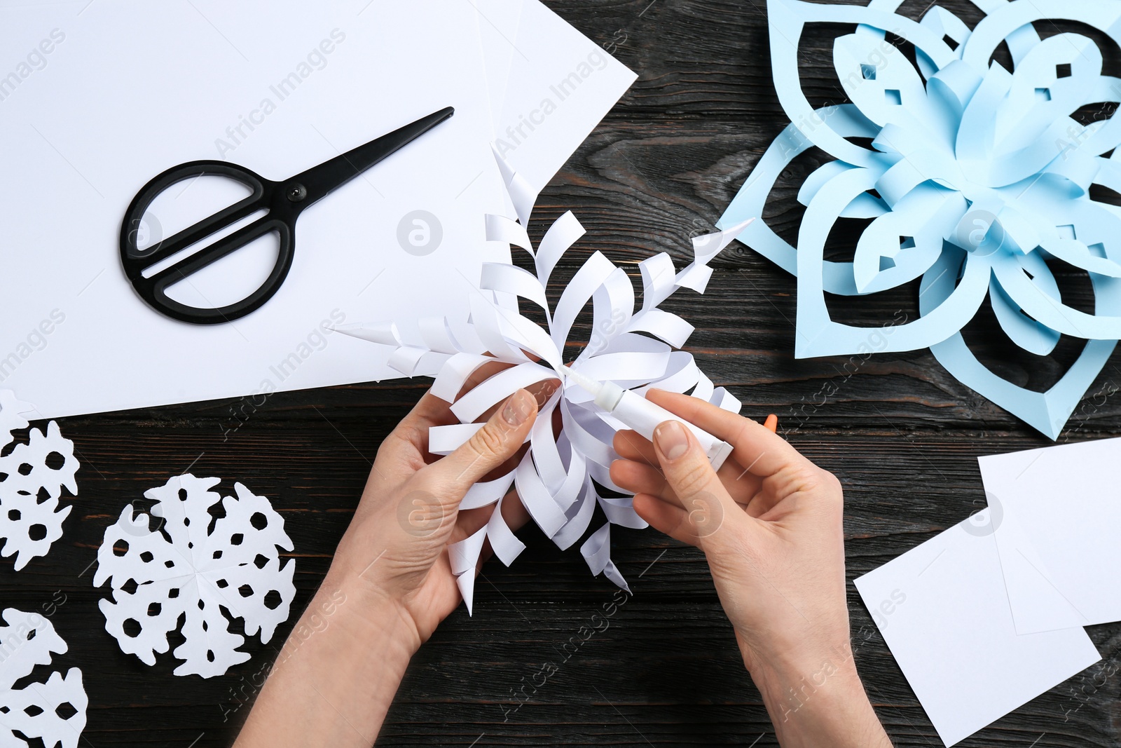 Photo of Woman making paper snowflake at black wooden table, top view