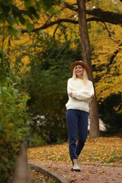 Photo of Happy woman wearing warm sweater walking in autumn park