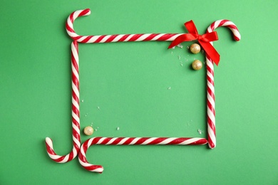 Photo of Frame made of candy canes on green background, top view. Space for text