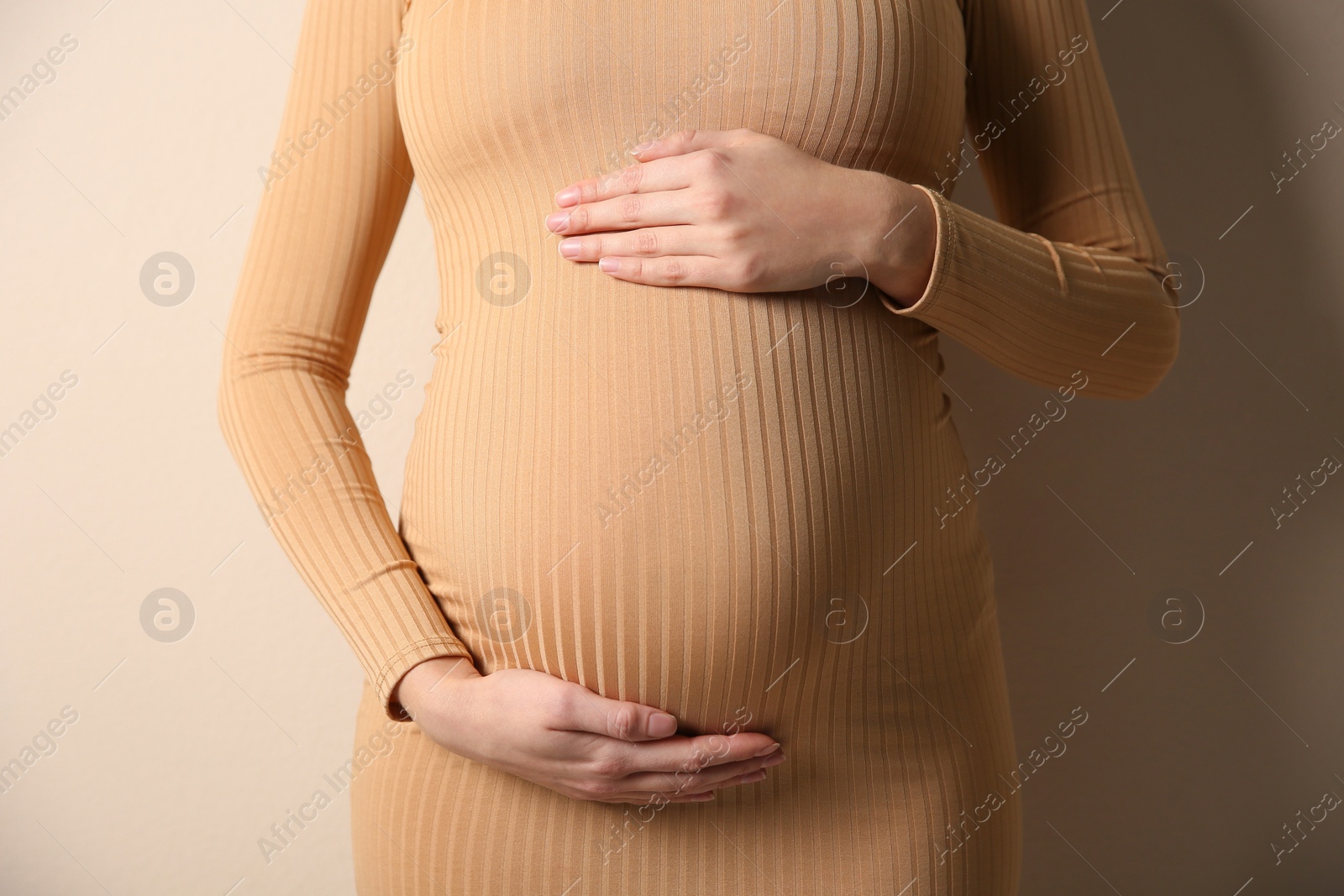 Photo of Pregnant woman touching her belly on beige background, closeup