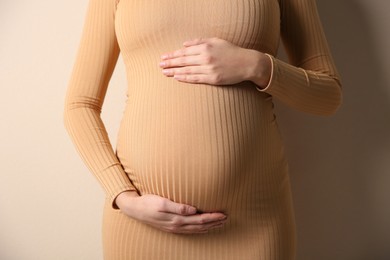 Photo of Pregnant woman touching her belly on beige background, closeup