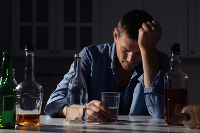 Photo of Addicted man with alcoholic drink at table in kitchen