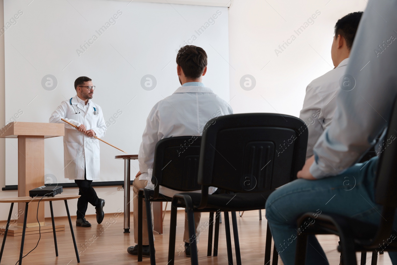 Photo of Doctor giving lecture in conference room with projection screen