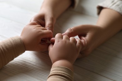 Photo of Woman holding hands with her little daughter at white wooden table, closeup
