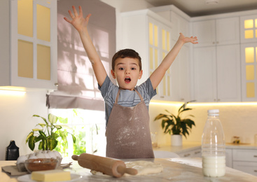 Photo of Emotional little boy at table with cooking ingredients in kitchen
