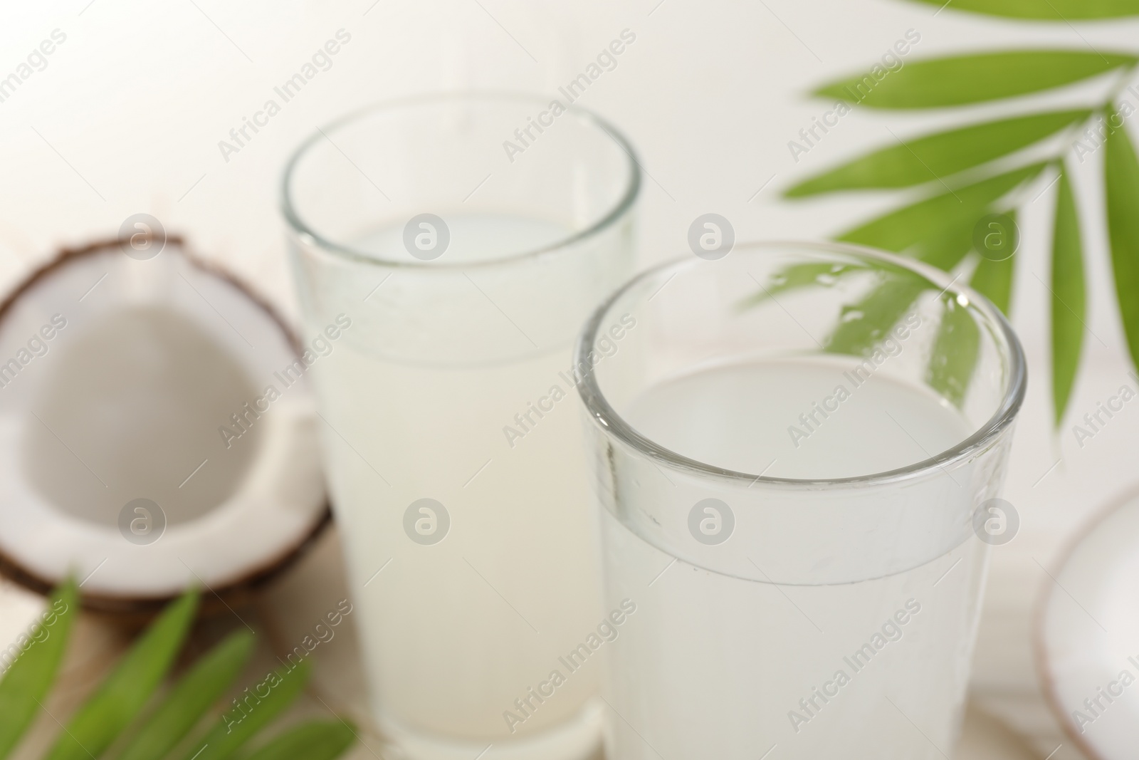 Photo of Glasses of coconut water, palm leaves and nuts on white table, closeup