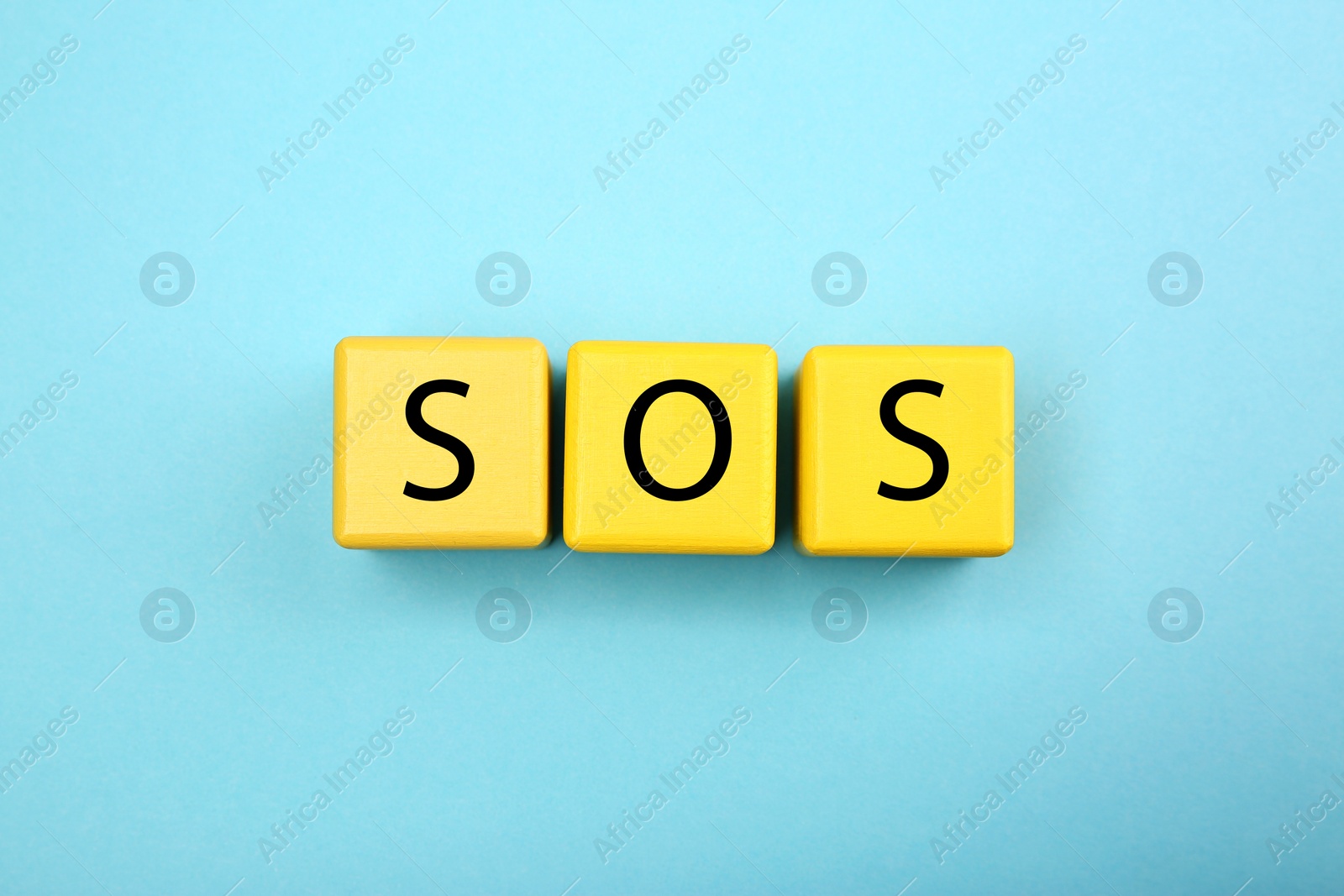 Photo of Abbreviation SOS (Save Our Souls) made of yellow cubes with letters on light blue background, top view