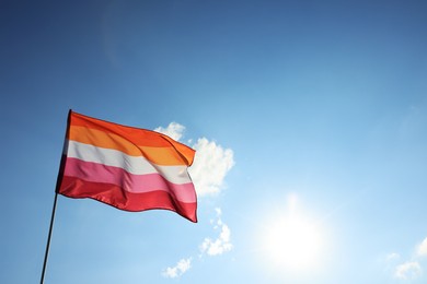 Photo of Bright lesbian flag fluttering against blue sky. Space for text