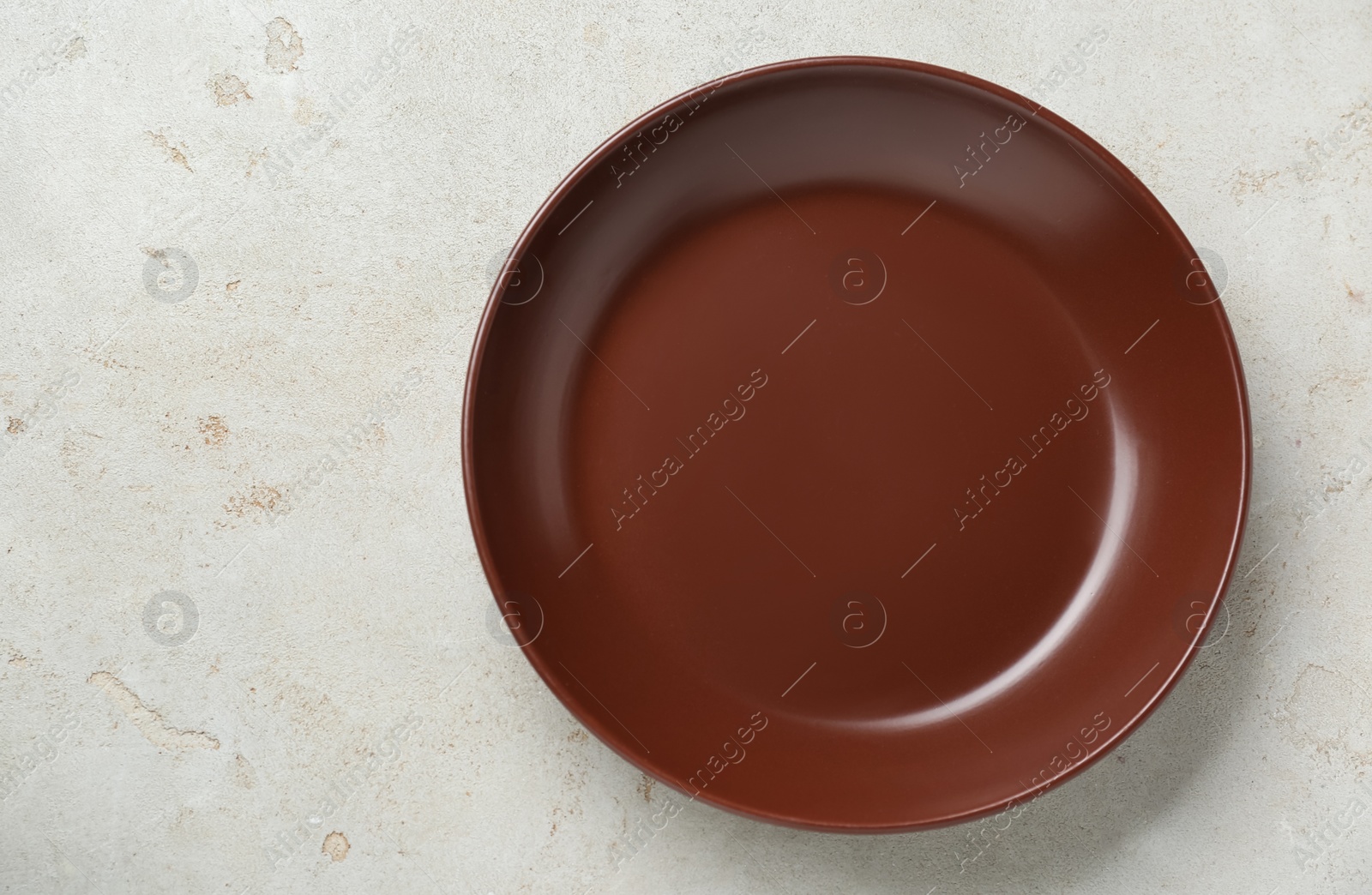 Photo of Empty brown ceramic plate on light grey table, top view. Space for text