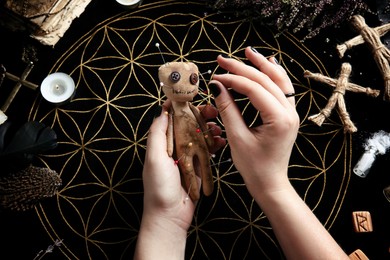 Woman stabbing voodoo doll with needle at table, closeup. Curse ceremony