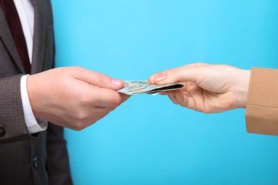 Photo of Man giving money to woman on light blue background, closeup. Currency exchange