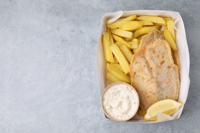 Photo of Delicious fish and chips with tasty sauce in paper box on gray table, top view. Space for text