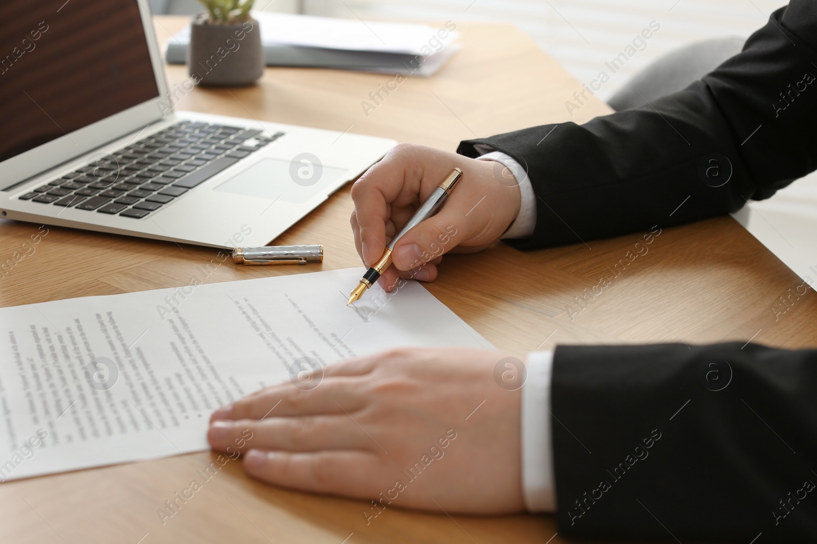 Photo of Notary signing document at wooden table, closeup