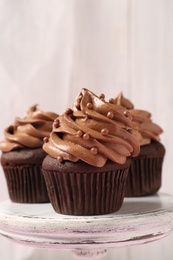 Photo of Delicious chocolate cupcakes with cream and beads on white stand, closeup