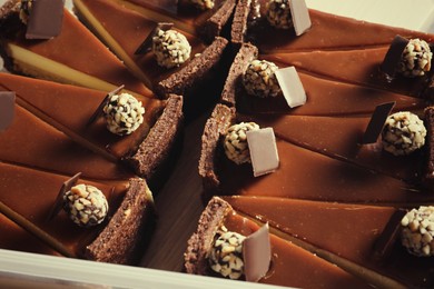 Photo of Pieces of delicious cheesecake with caramel and chocolate candies in box, above view
