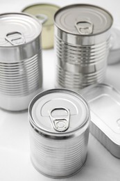 Many closed tin cans on white tiled table, closeup