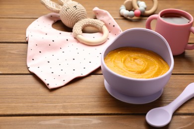 Plastic dishware with healthy baby food on wooden table. Space for text