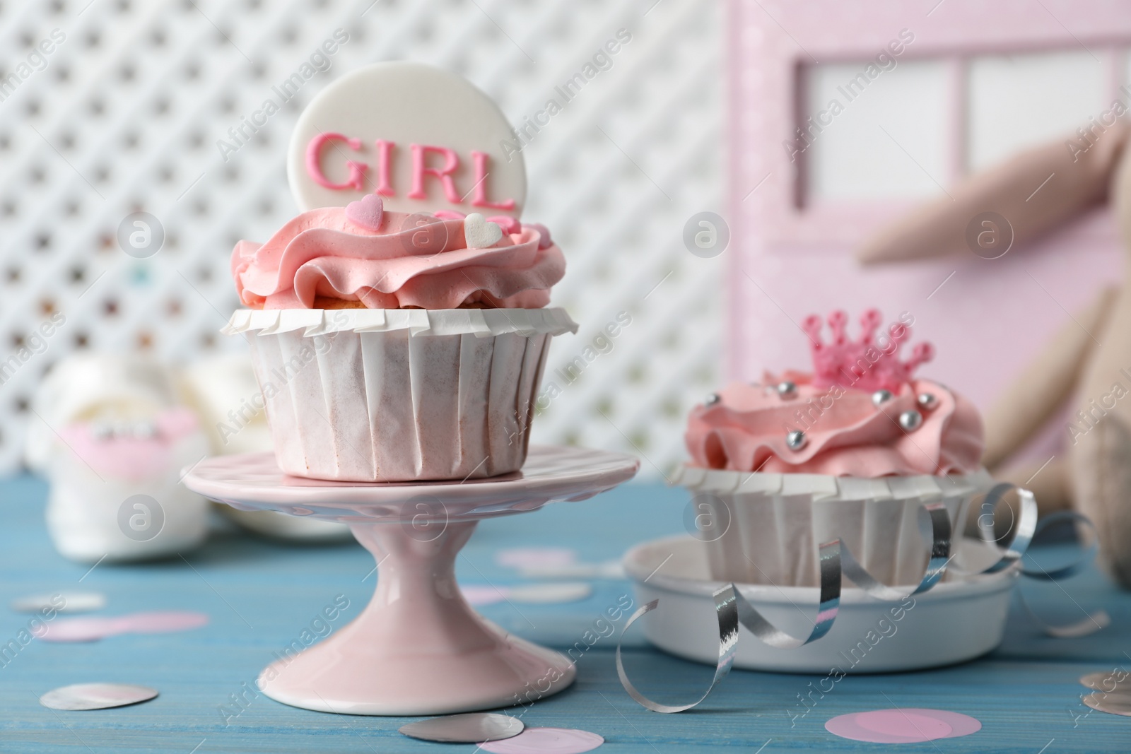 Photo of Delicious cupcakes with pink cream and toppers for baby shower on light blue wooden table