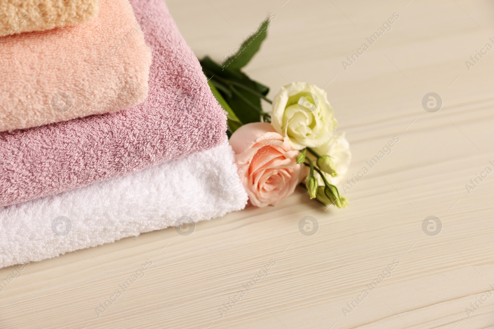 Photo of Soft folded towels, rose and eustoma flowers on light wooden table, closeup