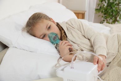 Photo of Little girl using nebulizer for inhalation on bed at home