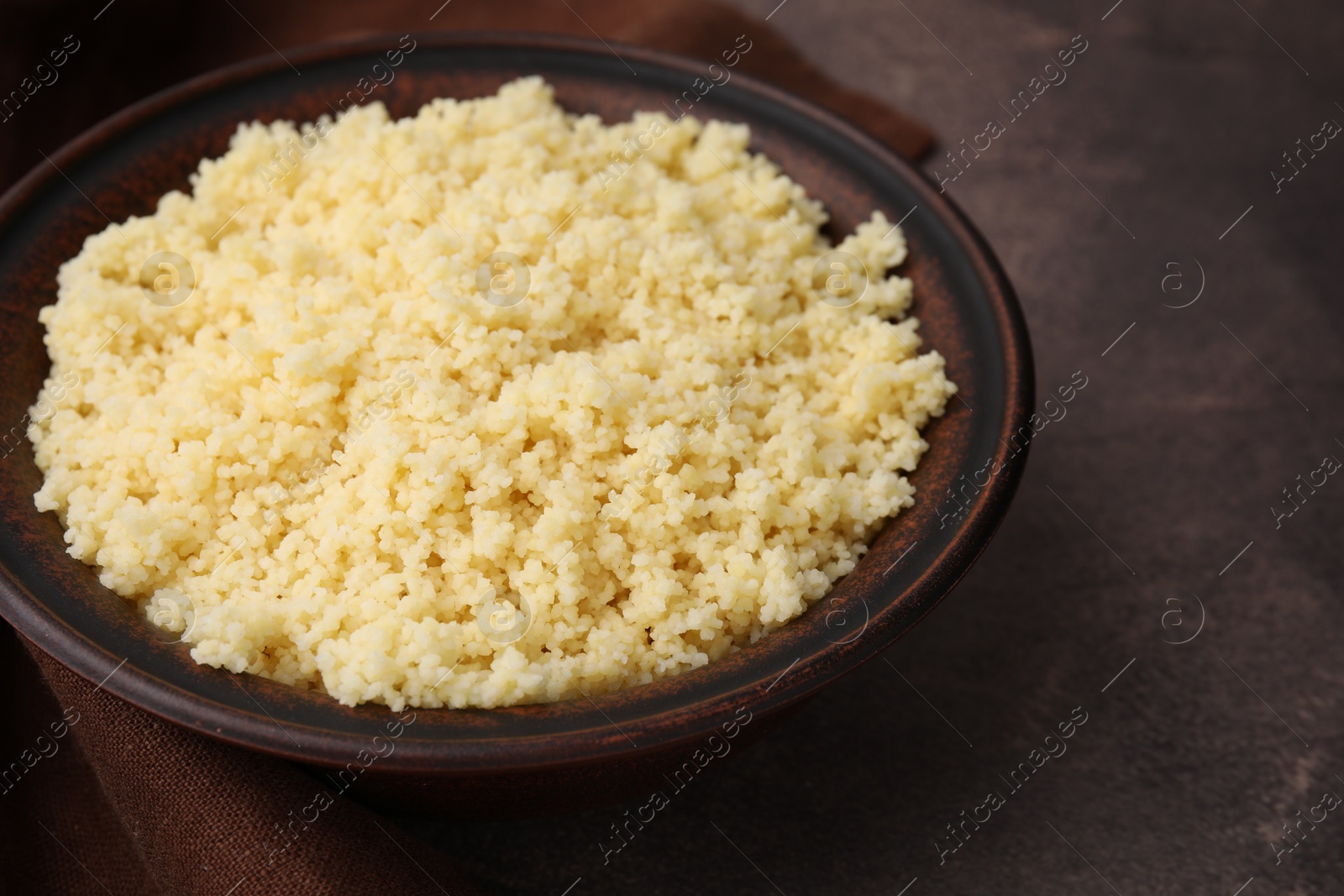 Photo of Tasty couscous in bowl on brown table, closeup. Space for text