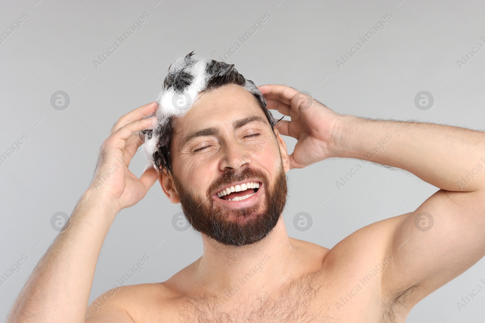 Photo of Happy man washing his hair with shampoo on grey background, closeup