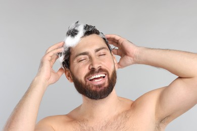 Happy man washing his hair with shampoo on grey background, closeup