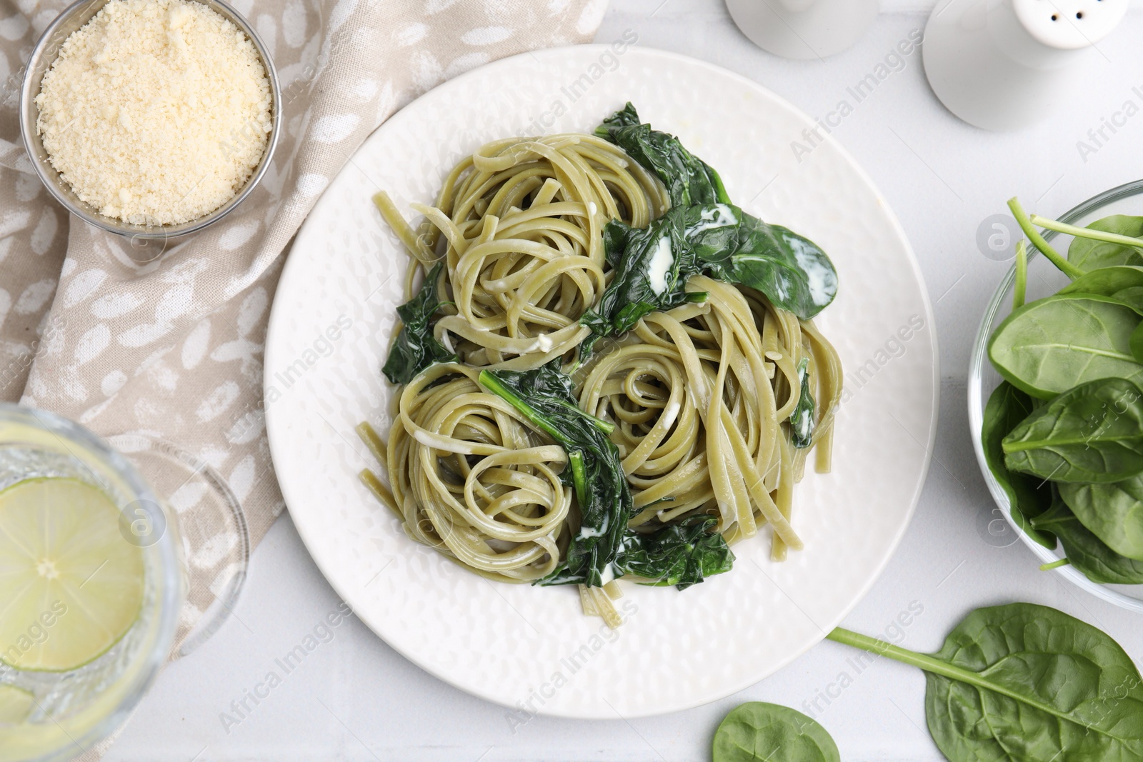 Photo of Tasty pasta with spinach and sauce served on white tiled table, flat lay