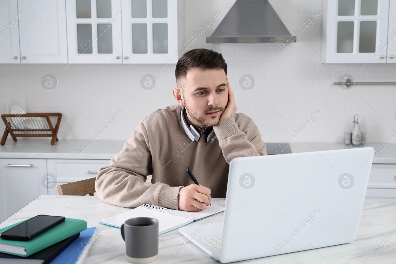 Photo of Young man using modern laptop for studying in kitchen. Distance learning